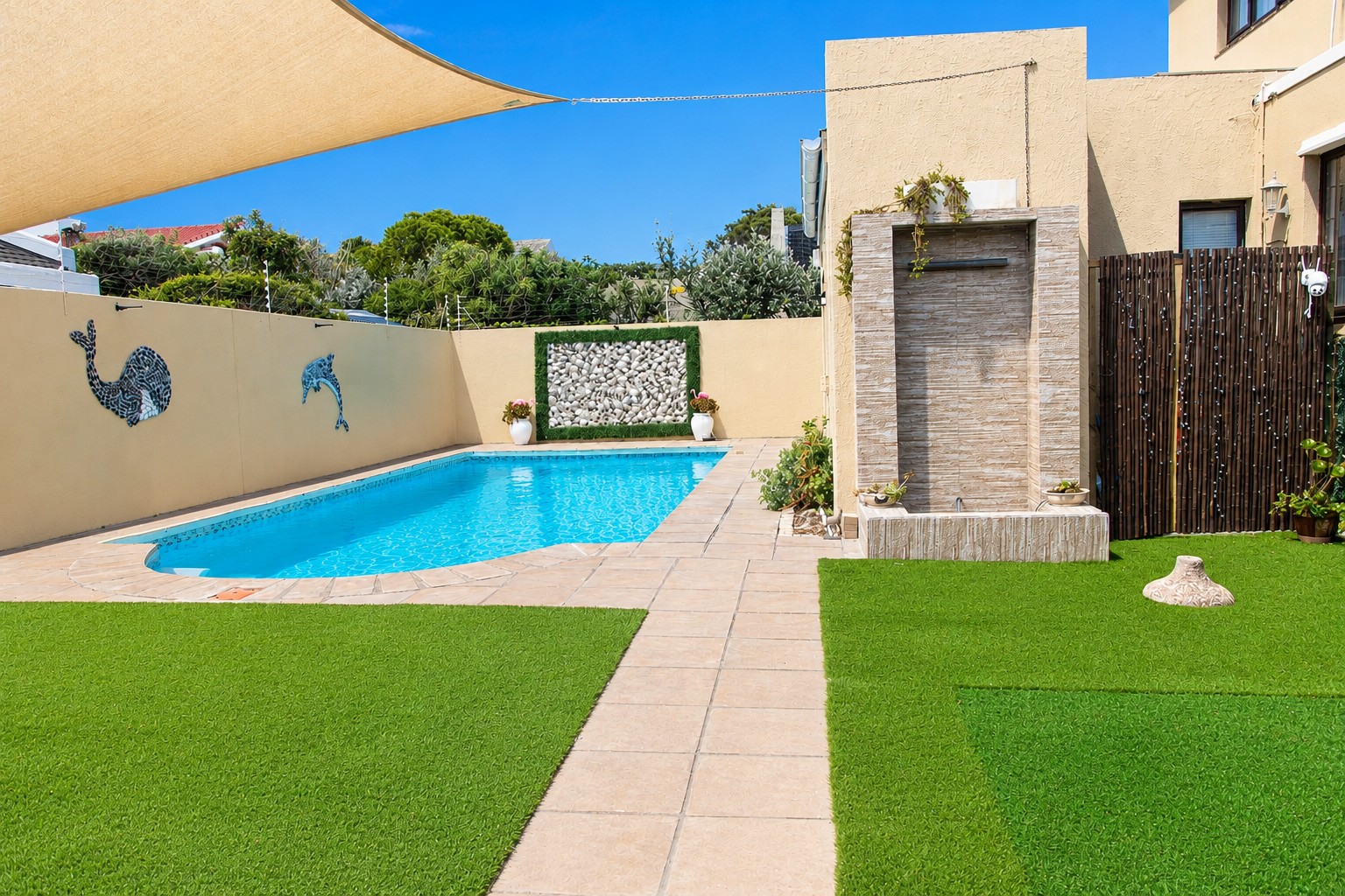 Full-size private pool with shade sail, artificial lawn, water feature and whale and dolphin mosaics